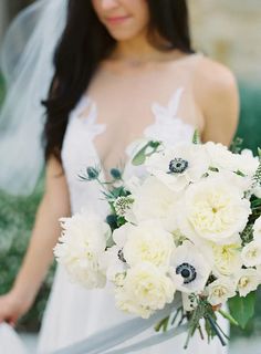 a woman in a wedding dress holding a bridal bouquet with white and black flowers