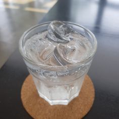 a glass filled with ice sitting on top of a wooden coaster