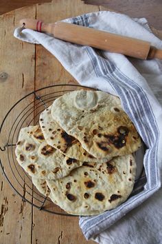 several flat breads on a wire rack with a rolling pin next to it and a towel