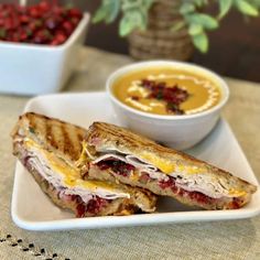 a sandwich cut in half sitting on top of a white plate next to a bowl of soup