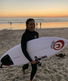 a woman holding a white surfboard on top of a sandy beach next to the ocean