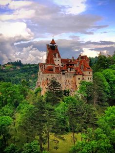 an old castle sitting on top of a hill surrounded by trees and clouds in the sky