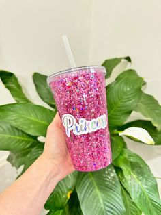 a hand holding a pink glittered cup with the word princess on it and a straw