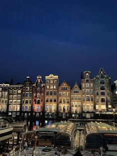 several boats are docked in front of some buildings at night time with the lights on