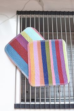 three multicolored dishcloths are hanging on a grill grate in front of a window