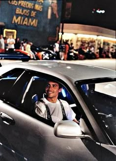 a man sitting in the driver's seat of a silver sports car at night