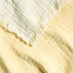 the blanket is white and yellow with fringes on it's edges, as well as an unmade bed spread