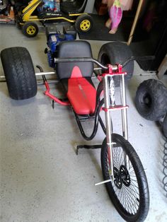 a red and black tricycle sitting on top of a garage floor next to tires