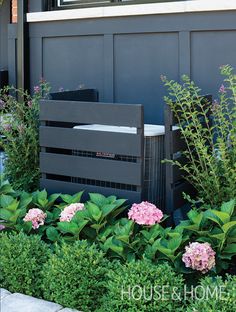 an air conditioner sitting in the middle of some bushes and flowers next to a building