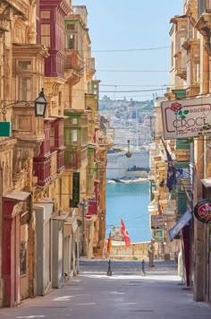 a narrow street with lots of buildings on both sides and a body of water in the distance