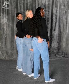 three women are standing in front of a backdrop wearing ripped jeans and black sweaters