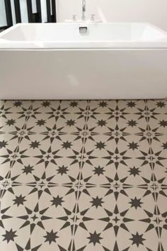 a bath tub sitting next to a black and white tiled floor in a bathroom with an ornate pattern on the floor