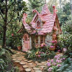 a small pink house in the middle of some flowers and trees with lots of plants around it