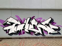 graffiti on the side of a building with purple and white spray painted letters above it