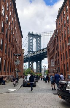 people walking and riding bikes on a city street with the manhattan bridge in the background