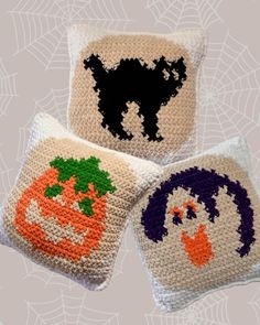 three crocheted pillows with faces and pumpkins on them, one is white