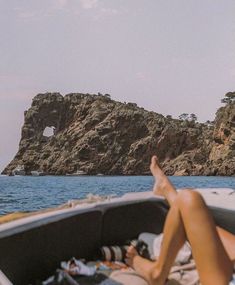 a person laying on the back of a boat in front of an island with rocks