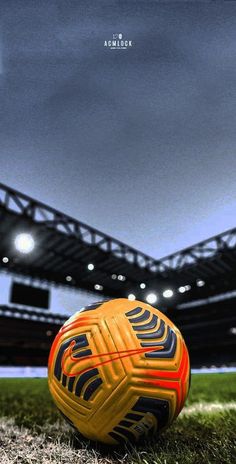 a yellow soccer ball sitting on top of a field in front of an empty stadium