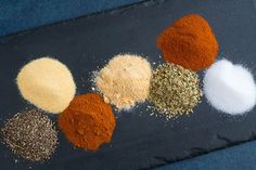 several different types of spices on a black tablecloth with blue cloth behind it, including red, yellow, and white