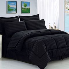 a bed with black comforter and pillows in a room next to a painting on the wall