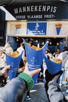 two people holding up blue cones in front of a food stand with other people standing around