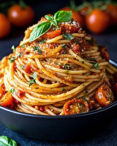 pasta with tomato sauce and basil leaves in a black bowl on a blue tablecloth