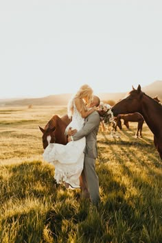 a bride and groom kissing in front of horses on a field at sunset with the sun behind them