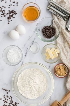 ingredients to make chocolate chip cookies laid out on a marble counter top with flour, butter, and eggs