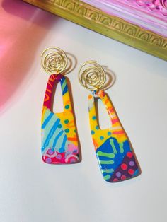 two pairs of colorful earrings sitting on top of a white table next to a gold frame