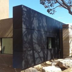 a black building sitting on the side of a road next to rocks and a tree