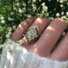 a person's hand with a ring on it and flowers in the back ground