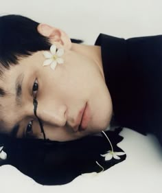 a young man laying on the ground with his eyes closed and flowers in his hair