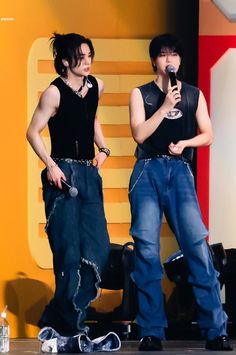 two young men standing on stage one holding a microphone and the other singing into a microphone