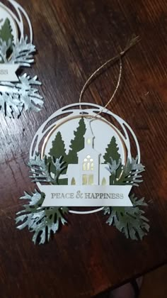 two christmas ornament hanging on a table with snowflakes and evergreens