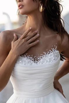 a woman wearing a wedding dress with pearls on the chest and shoulder, holding her hands to her chest