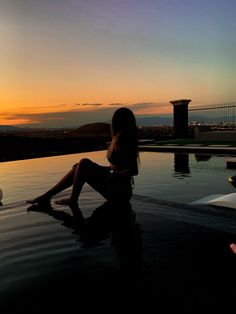 a woman sitting on the edge of a swimming pool at sunset