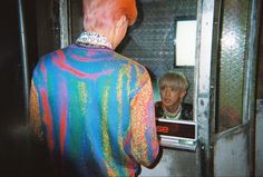 a man with red hair is looking at his reflection in the mirror while wearing a colorful jacket