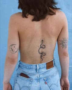 the back of a woman with tattoos on her upper and lower body, wearing blue jeans