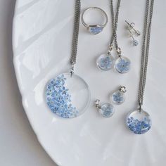 four pieces of jewelry on a plate with silver chains and blue flowers in the center