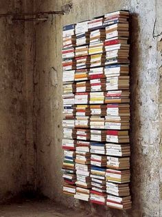 a large stack of books sitting on top of a cement floor next to a wall