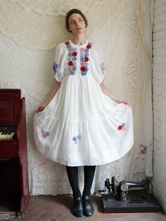 a woman in a white dress standing next to an old fashioned sewing machine with her hands on her hips