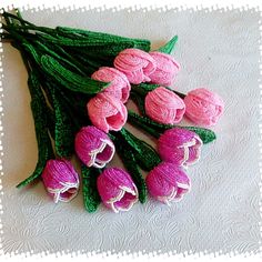 some pink flowers are laying on a white table cloth and green stems have been crocheted