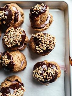 chocolate covered donuts with nuts and sprinkles on top sitting on a baking sheet