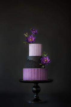 a three tiered cake with purple flowers on the top and black stripes around it