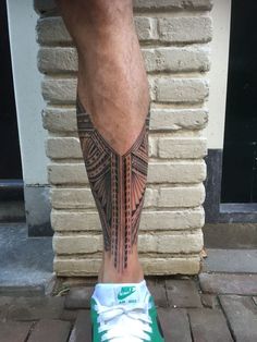 a man's leg with a tattoo on it and his green sneakers in front of a brick wall