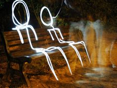 two people are sitting on a bench with their hands in the air while light is projected over them