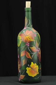 a green vase with yellow and red flowers painted on the side, sitting on a black surface