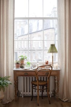 a wooden desk sitting under a large window next to a lamp and potted plant