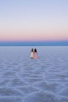 two girls standing in the middle of a vast expanse of water at sunset or dawn