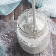 a glass jar filled with whipped cream on top of a wooden table covered in plastic wrap